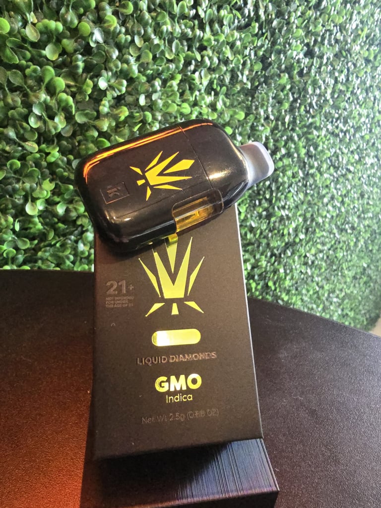 Black and gold Liquid Diamonds GMO indica cannabis cartridge box with crown logo displayed on green textured background