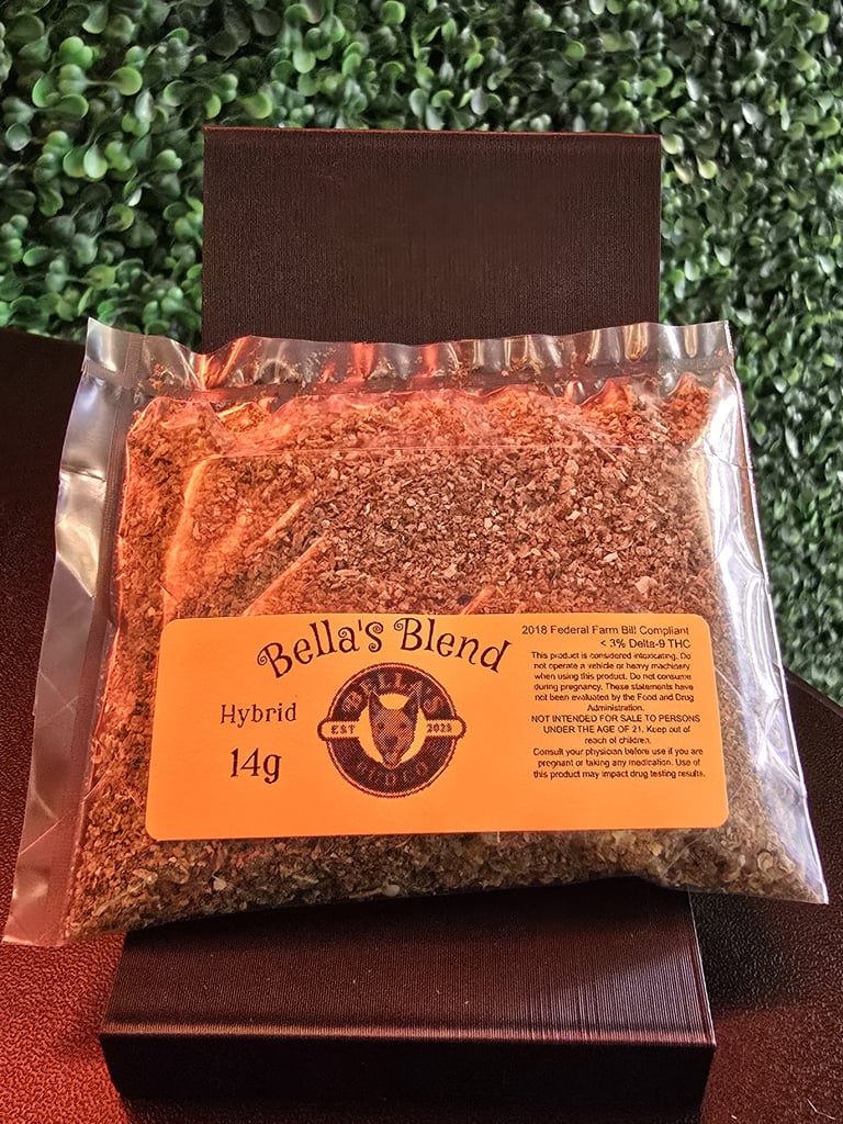 Bellas Blend hybrid chili powder in a 14g clear bag with orange label on brown background against green leafy backdrop