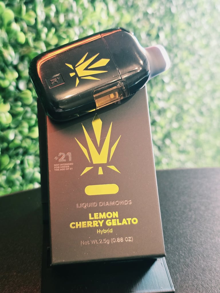 A black and gold Liquid Diamonds vape cartridge labeled Lemon Cherry Gelato Hybrid displayed on its packaging box with a green leafy background.
