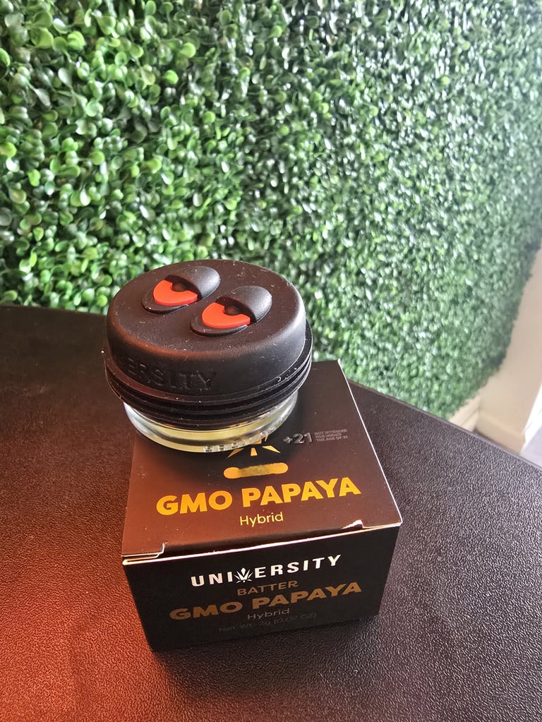 GMO Papaya Hybrid cannabis strain container with black lid and orange heart design on brown box against green plant background