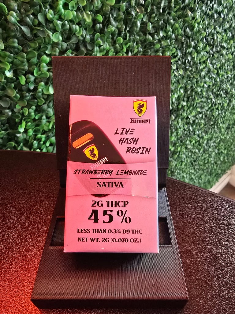 Pink cannabis product package labeled Ferrari with live hash rosin, strawberry lemonade sativa strain, 45% THCP, displayed on dark wooden surface with greenery background
