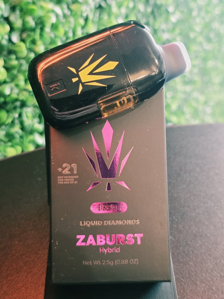 Black vape cartridge labeled Zaburst Hybrid with pink and gold crown design, sitting atop product packaging box with green background