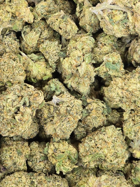 Close-up view of multiple dried cannabis flower buds covered in crystalline trichomes, displaying green and pale coloring